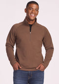 A smiling man wears the Woolx Blizzard 1/4 Zip in Bourbon Oak and blue jeans, standing with his hands in his pockets against a light background.