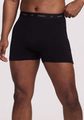 A person is wearing Breathe Boxer Shorts - Black from Woolx, featuring a "woolx" waistband, highlighting the breathability of Australian Merino Wool. The image shows them from mid-thigh to the waist against a plain background. | Trell is 6’2”, wearing a size M