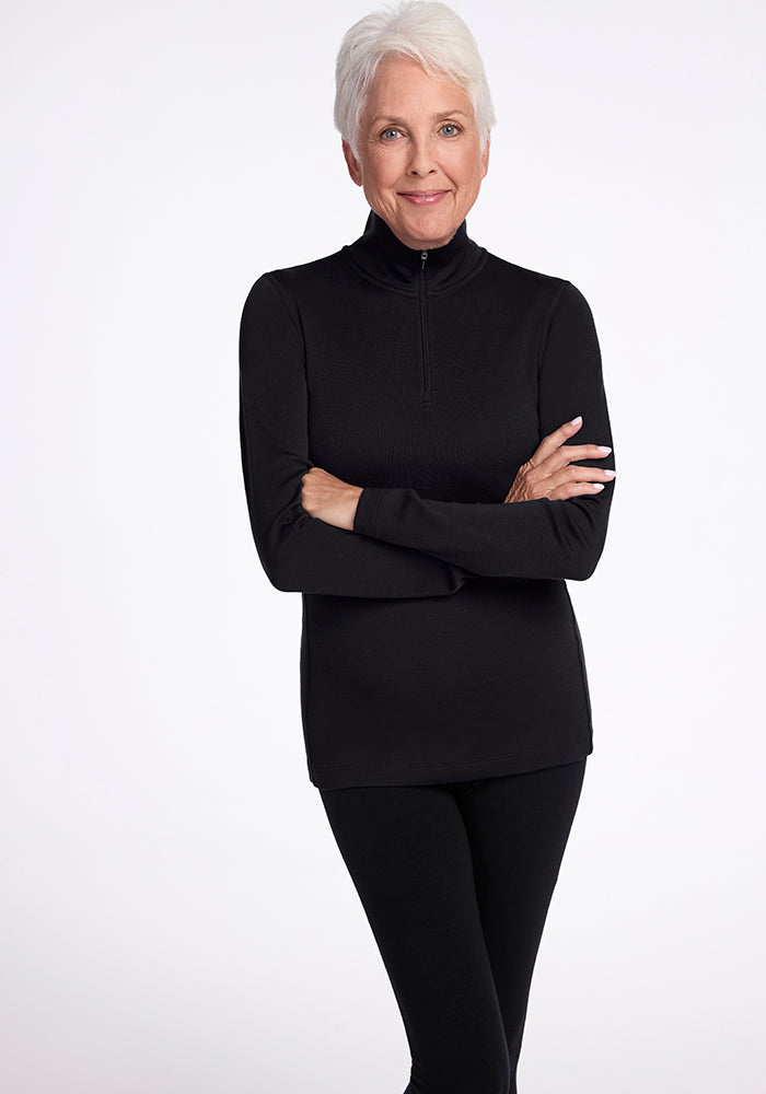 An older adult with short white hair is wearing the Woolx Brooke 1/4 Zip top and black pants, standing against a plain white background with arms crossed, smiling gently at the camera. | Kathy is 5'8", wearing a size S