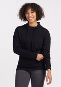 A person with curly hair is smiling while wearing a cozy Callie Hoodie - Black from Woolx and gray leggings. They are standing against a plain white background with one hand touching their hip and the other resting on their stomach. | Tori is 5'7", wearing a size S