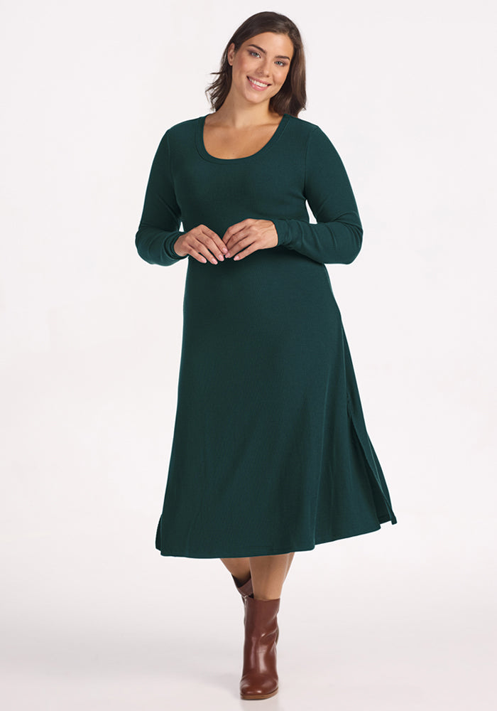 A woman in the Woolx Caroline Ribbed Twirl Dress in Deep Timber, paired with brown ankle boots, smiles against a plain white background. | Juliana is 5'10", wearing a size XL