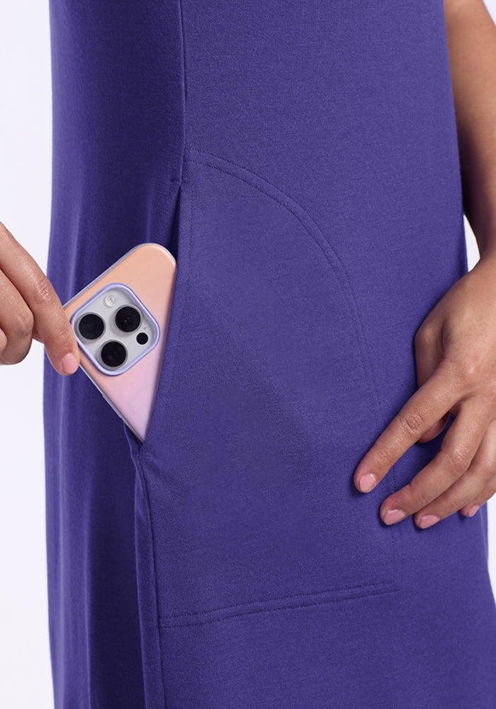 A person slips a smartphone into the side pocket of the Woolx Cassie Dress - Berry Indigo.