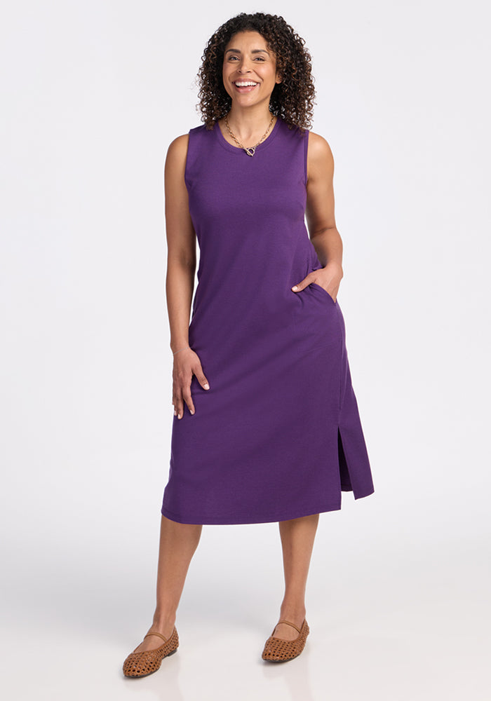 Woman in the Woolx Cassie Dress in Plum Crush, sleeveless, wrinkle-resistant, with side slit and hand in pocket.