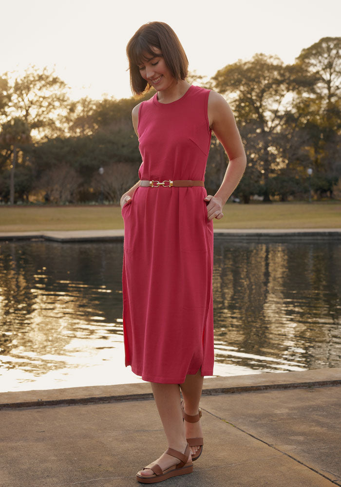 Woman in the Woolx Cassie Dress in Poppy Spark stands by a pond at sunset, smiling and looking down.