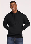 A young man smiles wearing the Woolx Chase Hoodie - Black, featuring moisture-wicking fabric and a front pocket, paired with blue jeans against a simple backdrop. | Trell is 6’2”, wearing a size M