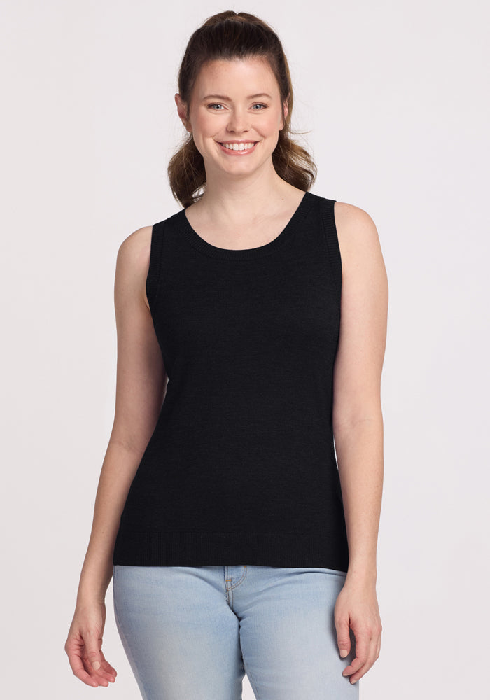 A woman with light skin and brown hair in a ponytail is smiling, wearing the Woolx Chessy Tank Top in black and light blue jeans, standing against a plain white background. | Lilly is 5’9”, wearing a size S