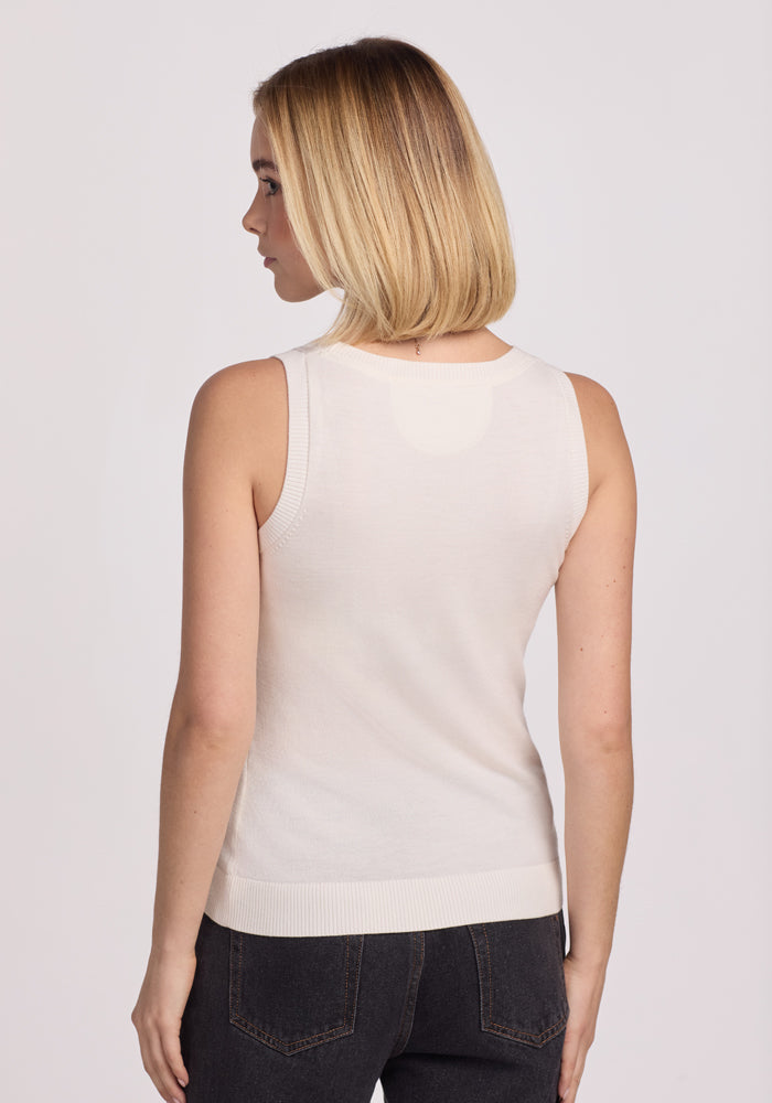 A person with shoulder-length blonde hair is viewed from behind, wearing a Woolx Chessy Tank Top in Dewdrop Pearl and dark jeans. The plain white background accentuates the casual outfit.