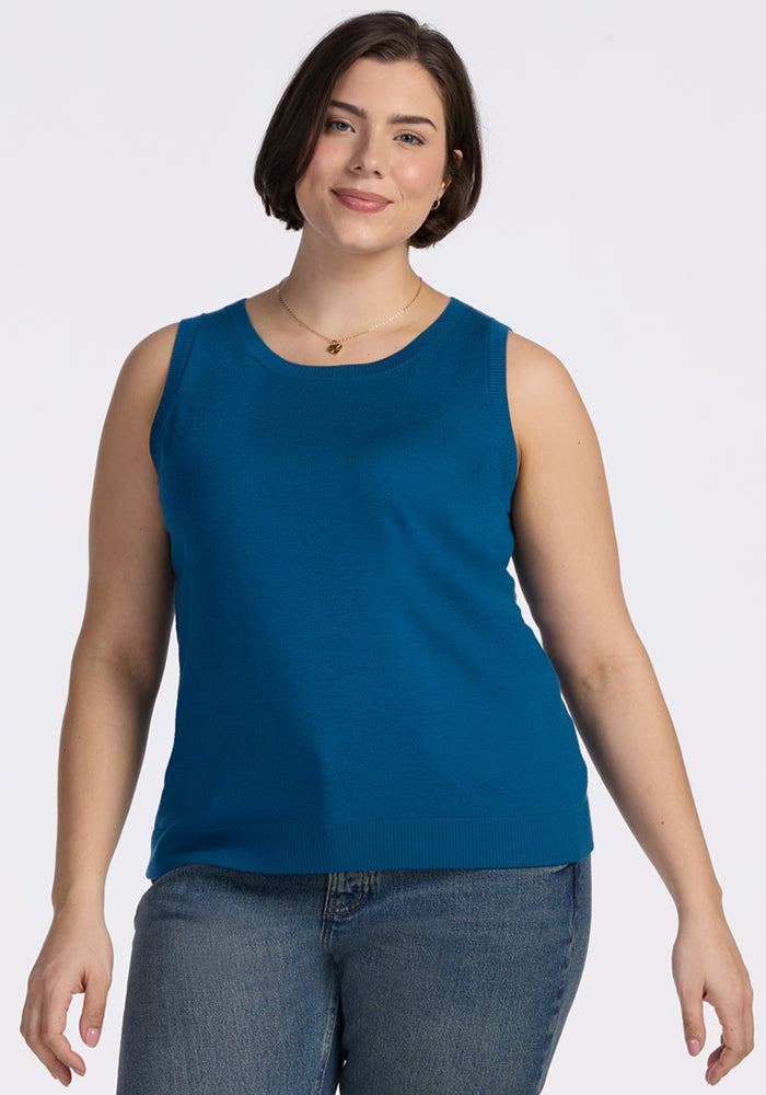 A woman with short brown hair, wearing the Woolx Chessy Tank Top in Moroccan Blue and blue jeans, stands against a plain white background, smiling gently at the camera. | Juliana is '10", wearing a size XL