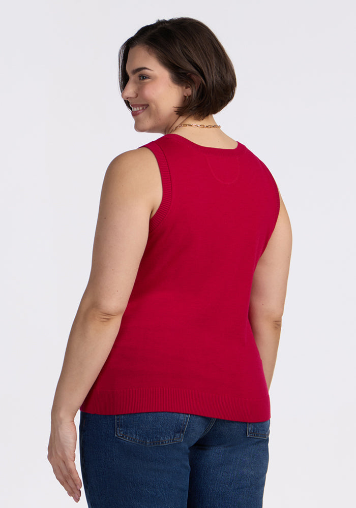 A woman with short brown hair, wearing the Woolx Chessy Tank Top in Poppy Spark and blue jeans, stands smiling over her shoulder against a plain light background.