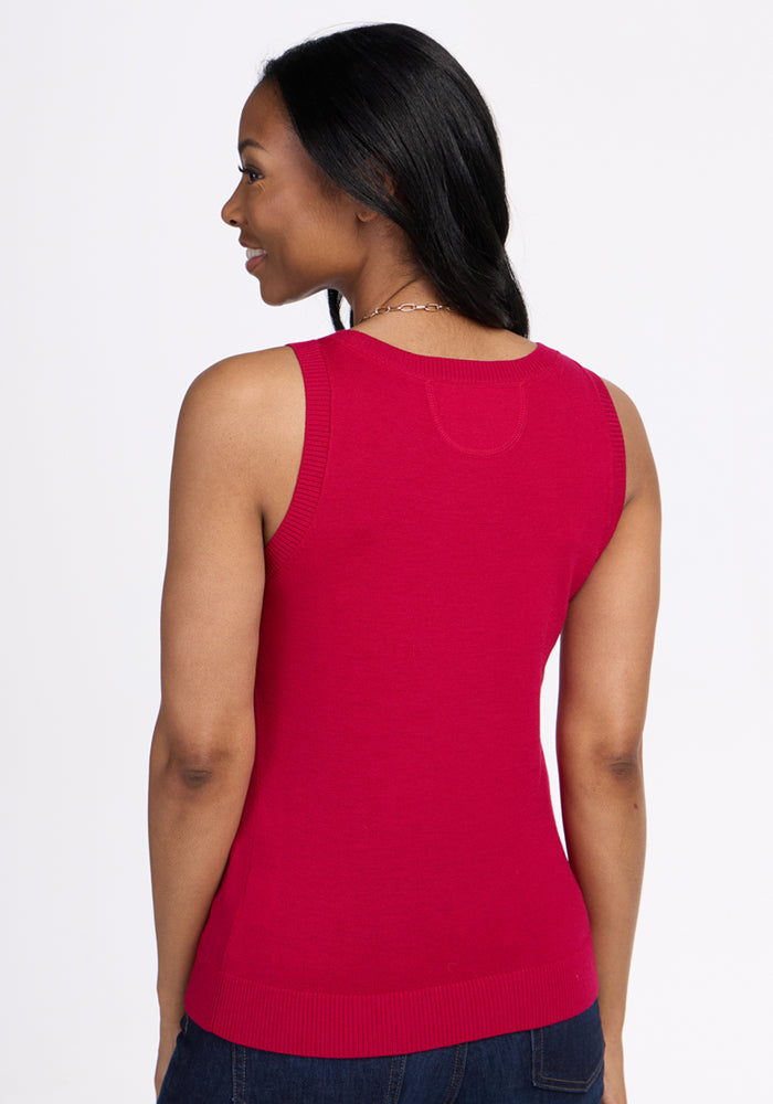 A woman with long dark hair wears the Woolx Chessy Tank Top in Poppy Spark and dark blue jeans, standing against a white background and smiling over her shoulder. This fitted merino wool tank is perfect for layering.
