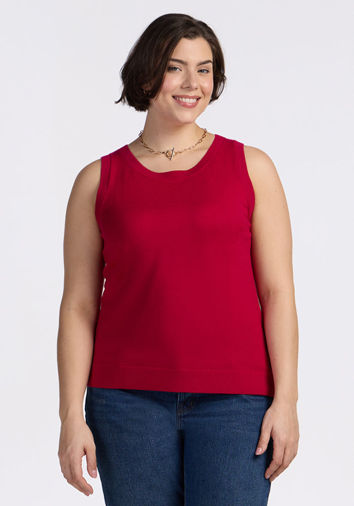 A woman with short brown hair wearing the Woolx Chessy Tank Top in Poppy Spark, blue jeans, and a necklace is smiling while standing against a plain white background. | Juliana is 5'10", wearing a size XL