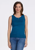 A woman with shoulder-length brown hair wears the Woolx Chessy Tank Top in Moroccan Blue, paired with blue jeans and a gold necklace, standing before a plain white background and smiling slightly. | Jessica is 5’10”, wearing a size S