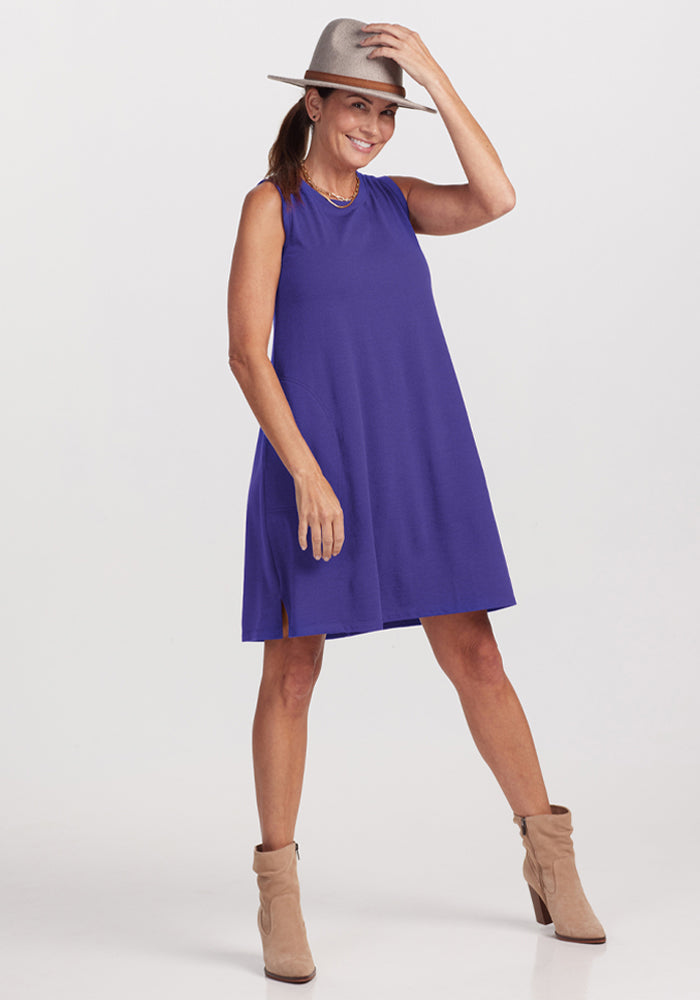 Woman in a Woolx Clara Dress - Berry Indigo, tan boots, and gray hat poses smiling against a white background.