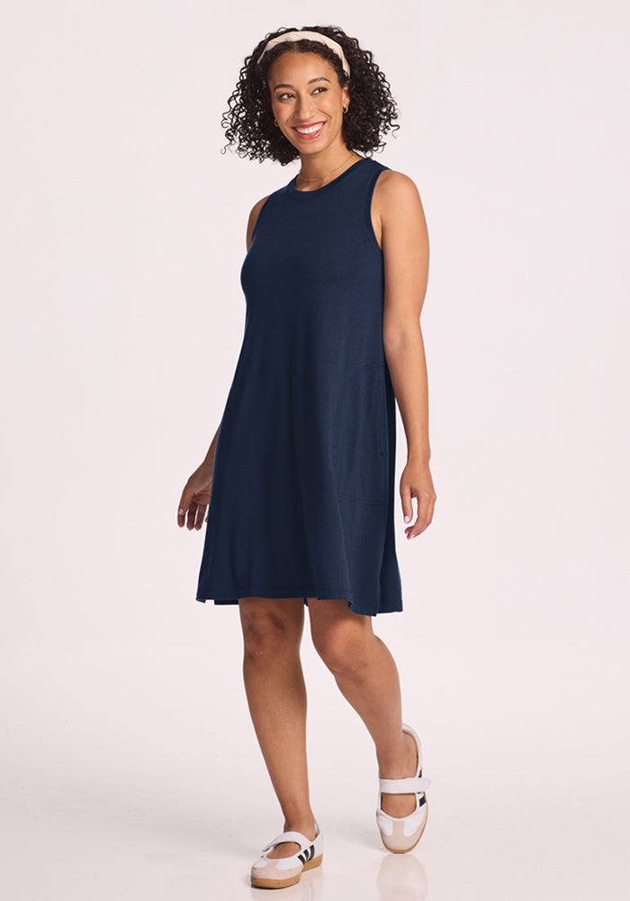 Woman in the Woolx Clara Dress in Deep Navy, smiling with a white headband and sandals against a plain background.