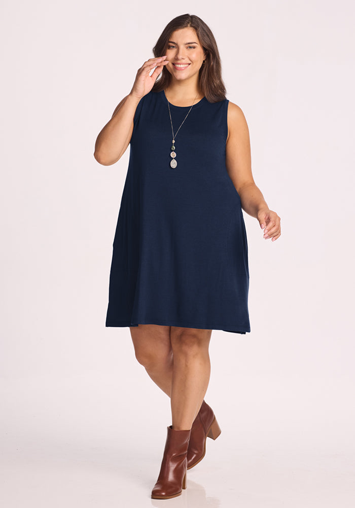 Woman in a Woolx Clara Dress in Deep Navy, brown ankle boots, and pendant necklace, smiling while walking.