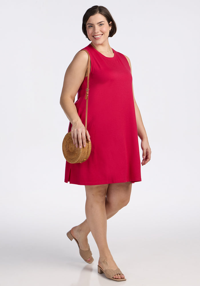 Woman in the Clara Dress by Woolx, carrying a round straw bag, wearing sandals, smiling as she walks.