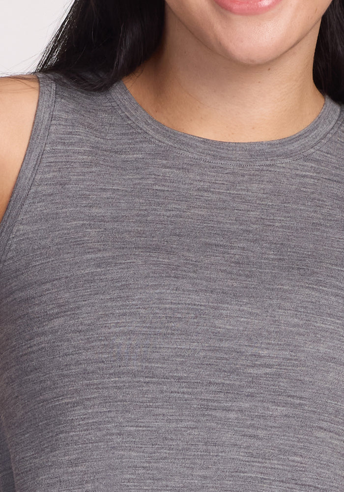 A person is shown wearing a Woolx Clara Dress in Graphite Heather, highlighting its smooth texture and odor-resistant fabric. Only part of their smile is visible from the shoulders down.