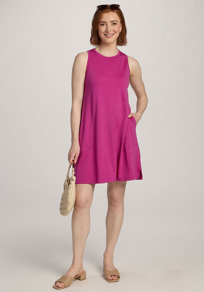 Smiling woman in the Woolx Clara Dress - Summer Sorbet, holding a beige purse and wearing sandals, stands against a plain background. | Shea is 5’9”, wearing a size S