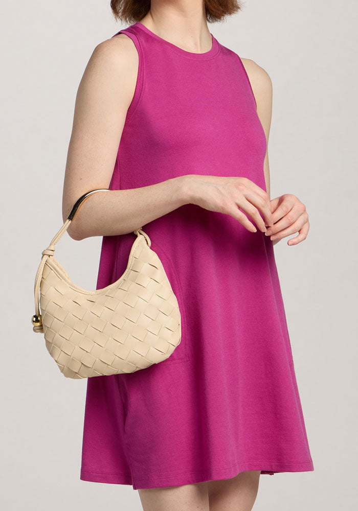 Woman in a Woolx Clara Dress - Summer Sorbet, holding a small woven beige handbag with short handle.