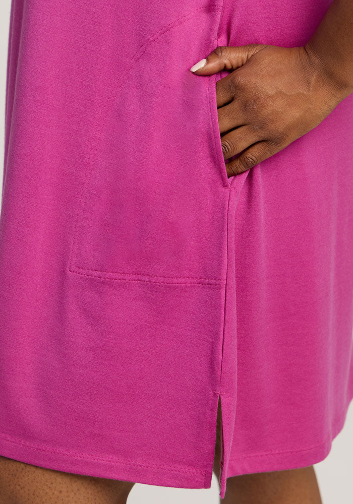 A hand rests in the pocket of the Woolx Clara Dress - Summer Sorbet, a bright pink, lightweight dress with a side slit.