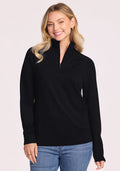 A woman with long blonde hair smiles, wearing the Woolx Collins Half Zip Sweater in black and blue jeans, standing against a plain light background. | Saige is 5'7", wearing a size XS