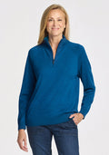 A woman with straight blonde hair smiles against a plain light background, wearing the Woolx Collins Half Zip Sweater in Moroccan Blue and blue jeans, with one hand in her pocket. | Andrea is 5’10”, wearing a size S