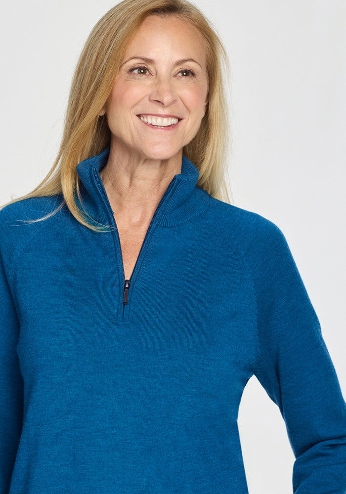 Smiling woman with long blonde hair wears the Woolx Collins Half Zip Sweater in Moroccan Blue, standing against a plain light background.
