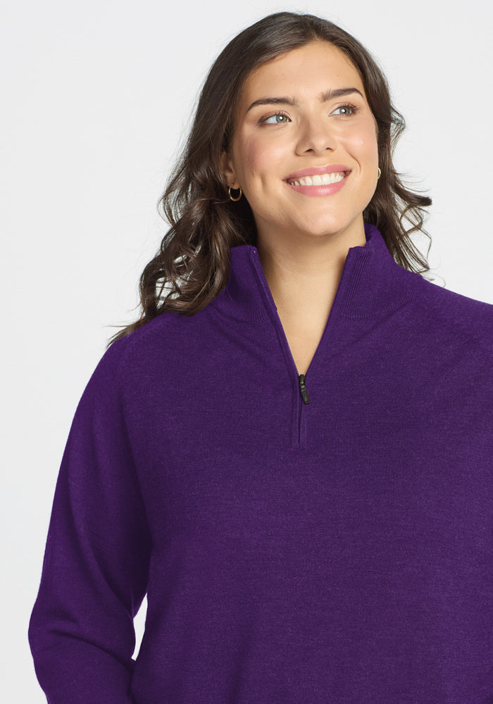A woman with wavy brown hair, wearing the Woolx Collins Half Zip Sweater in Plum Crush, smiles and looks slightly to her left against a plain white background.