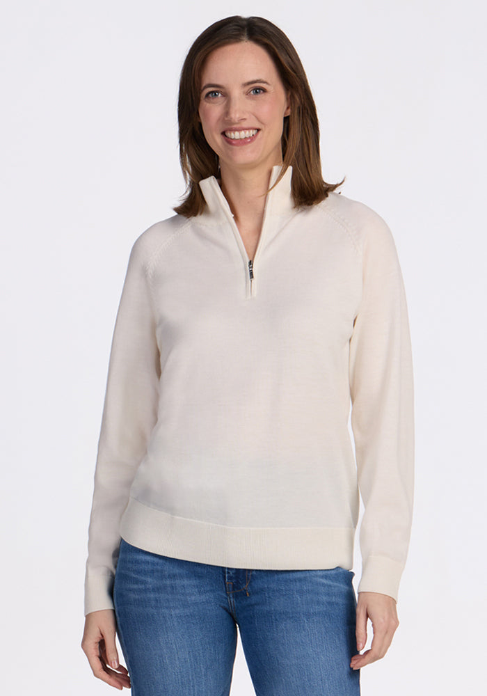 A woman with shoulder-length brown hair smiles while wearing the Woolx Collins Half Zip Sweater in Dewdrop Pearl and blue jeans, standing against a plain white background. | Jessica is 5’10”, wearing a size S