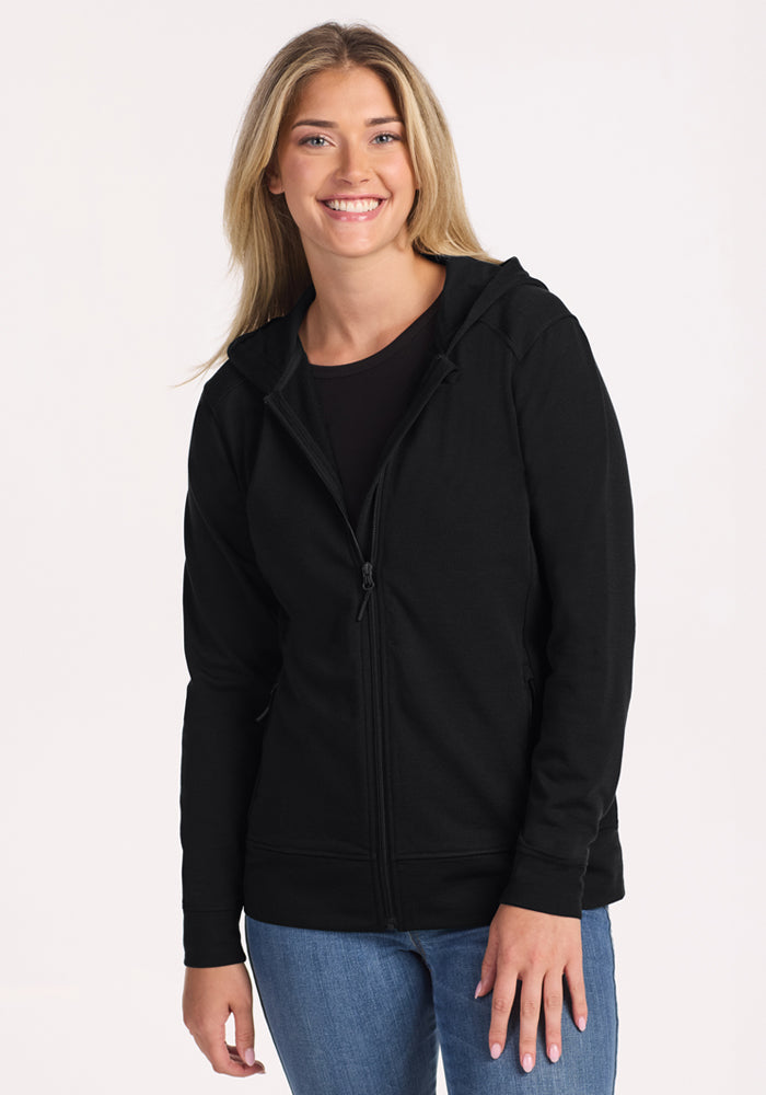 A smiling woman with long blonde hair wears the Woolx Darby Zip Up Hoodie in black over a black top and blue jeans, standing against a plain light background. | Ariana is 5'11", wearing a size S