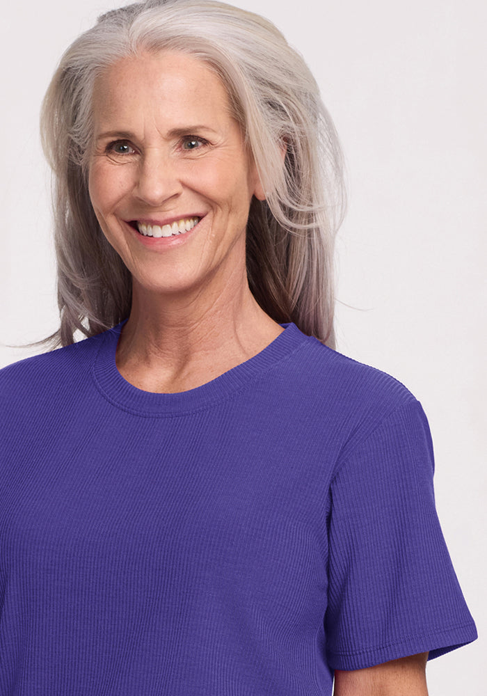 Smiling older woman wears Woolx Delia Ribbed Short Sleeve in Berry Indigo against a light background.
