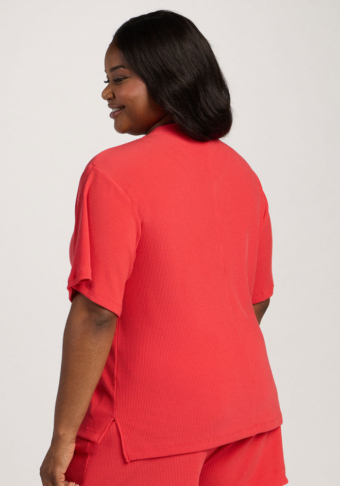A woman in the Woolx Delia Ribbed Short Sleeve - Hibiscus smiles, facing away from the camera in matching shorts.