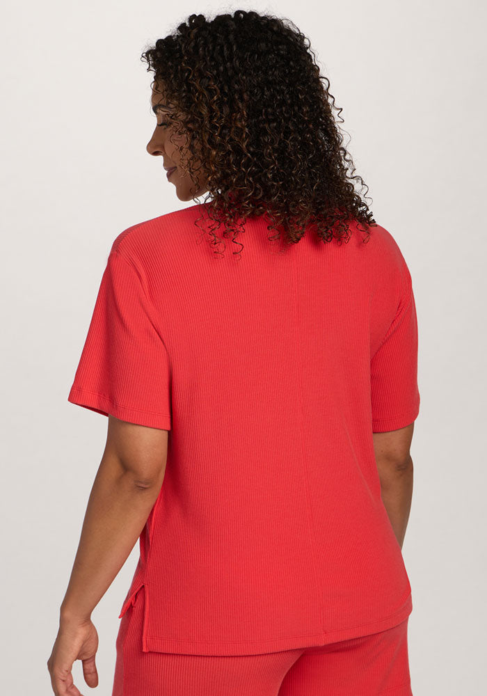 A woman with curly hair wears the Woolx Delia Ribbed Short Sleeve in Hibiscus, shown from the back.