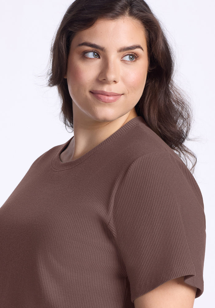 Woman with wavy brown hair smiles in the Woolx Delia Ribbed Short Sleeve - Peppercorn, looking off to the side.