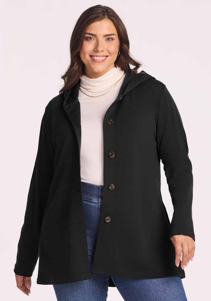 A woman with long brown hair, wearing a white turtleneck, blue jeans, and the Woolx Edna Hooded Cardigan in black, smiles while posing against a plain light background. | Juliana is 5'10", wearing a size XL