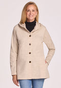 A smiling woman with long blonde hair wears the Woolx Edna Hooded Cardigan in Cream Heather over a black turtleneck and blue jeans, standing against a light background. This cozy piece is perfect for cold weather. | Andrea is 5'10", wearing a size S