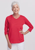 Smiling older woman in a Woolx Elena 3/4 Sleeve V Neck - Berry Ice Pop top and white pants, hand on her hip. | Kathy is 5’9”, wearing a size S