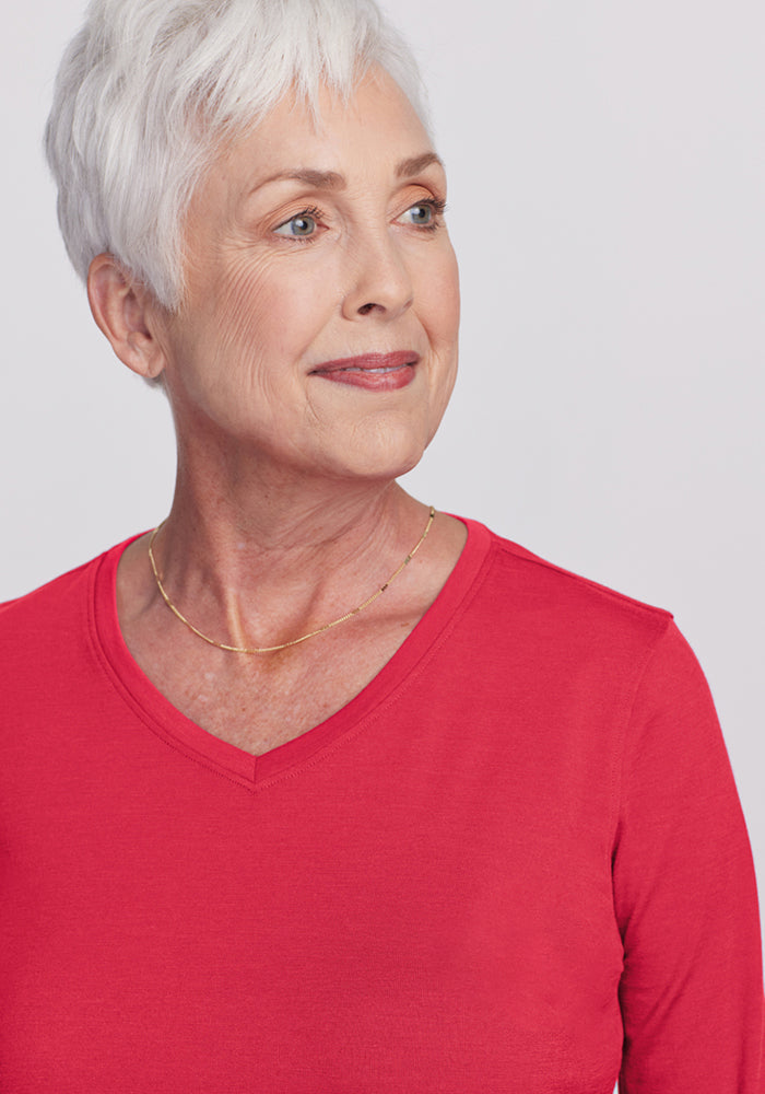 Older woman with short white hair wears Woolx Elena 3/4 Sleeve V Neck in Berry Ice Pop and a gold necklace, smiling gently.
