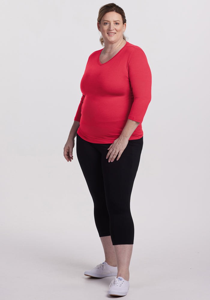 Woman wearing a Woolx Elena 3/4 Sleeve V Neck in Berry Ice Pop, black leggings, and white sneakers, smiling.