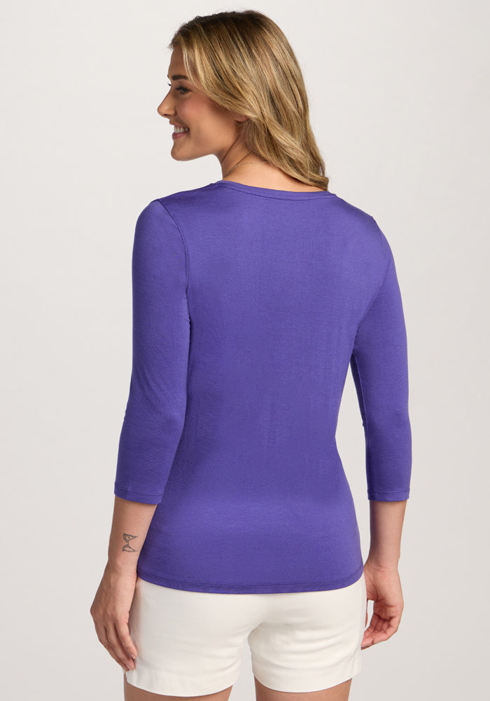 Woman smiles, facing away in Woolx Elena 3/4 Sleeve V Neck - Berry Indigo and white shorts, hands at her sides.