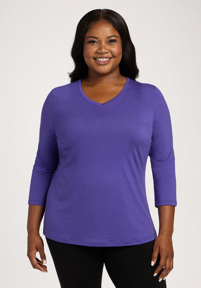 Smiling woman in a Woolx Elena 3/4 Sleeve V Neck - Berry Indigo and black pants, against a plain background. | Sapphire is 5’8”, wearing a size XL