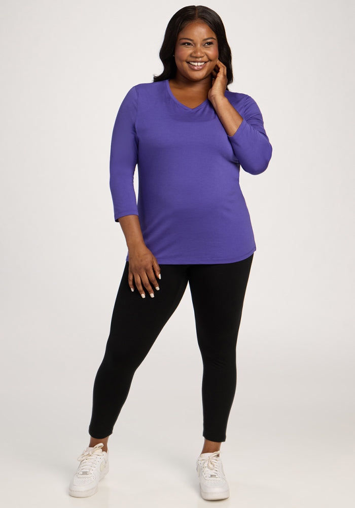 Woman smiling in Woolx Elena 3/4 Sleeve V Neck - Berry Indigo top, black leggings, and white sneakers.