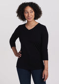 A person with curly hair poses confidently with a hand on their hip, showcasing casual chic in a black Woolx Elena 3/4 Sleeve V-Neck top and dark jeans against a plain white background. | Tori is 5'7", wearing a size S