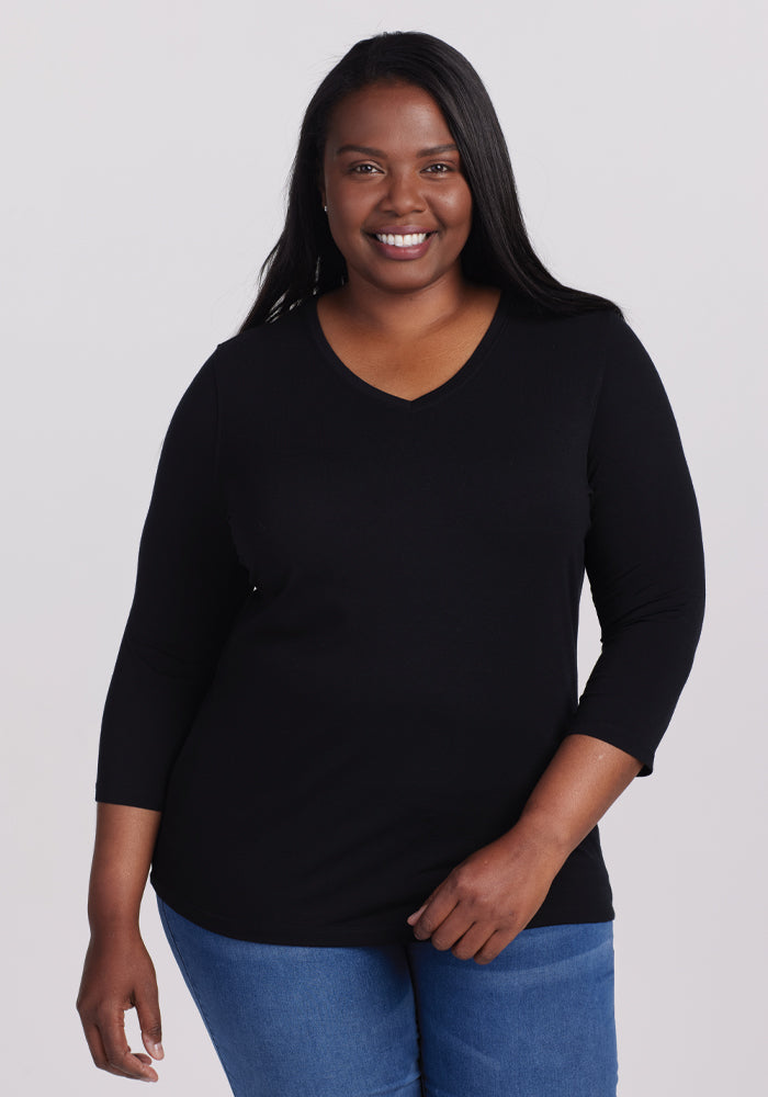 A smiling person with long black hair wears the versatile Woolx Elena 3/4 Sleeve V Neck in Black along with blue jeans, standing against a plain white background. | Le’Quita is 5’11”, wearing a size XL