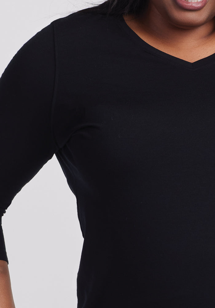 A close-up shows a person in a Woolx Elena 3/4 Sleeve V Neck - Black, highlighting this versatile wardrobe essential. The soft merino wool offers comfort, with only the torso and part of the head visible, featuring a warm smile against a plain background.