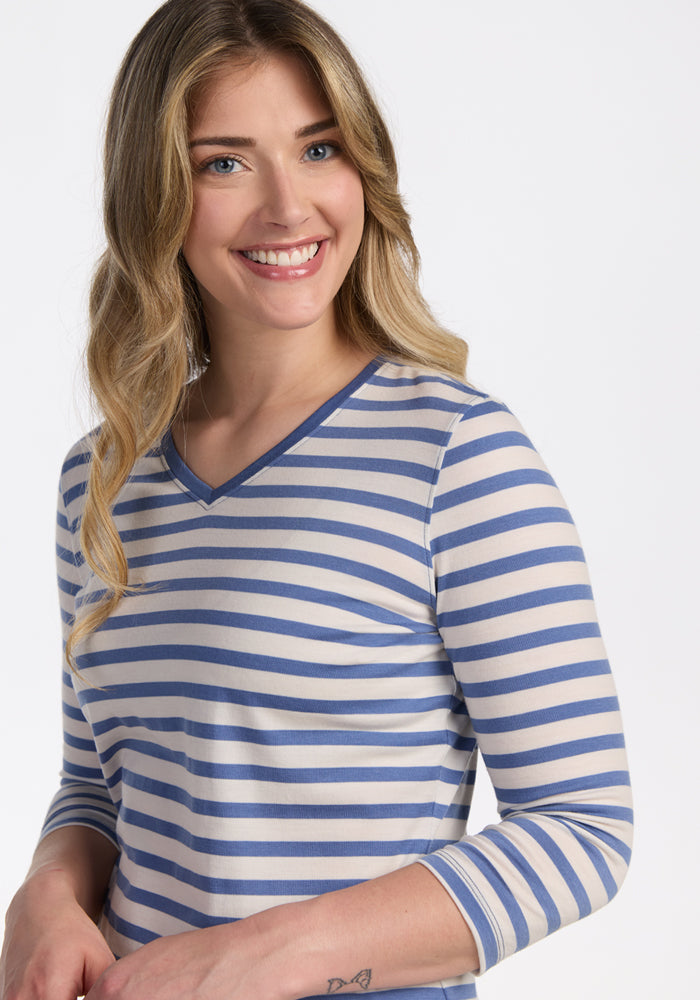 A smiling woman with long, wavy blonde hair wears the Woolx Elena 3/4 Sleeve V Neck in Blue Sand Stripe, posing against a plain white background.