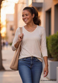 A smiling woman with a ponytail walks outside wearing the Woolx Elena 3/4 Sleeve V Neck in Cream Heather.