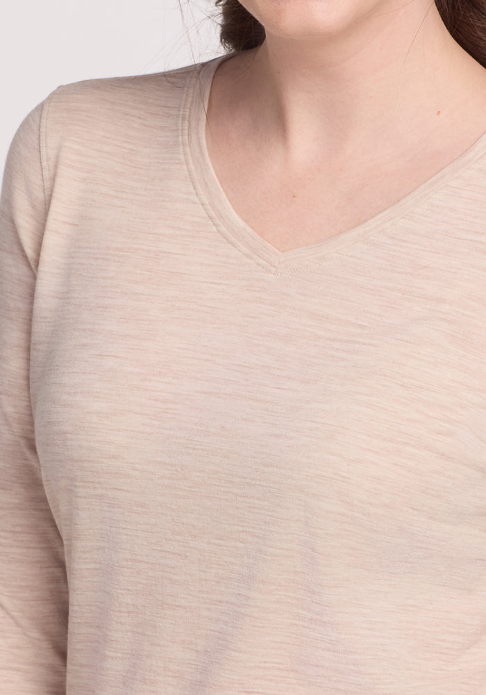 A close-up of a person in a cream heather Elena 3/4 Sleeve V Neck top by Woolx, highlighting its merino wool texture and modern chic style. Only the lower part of the person's face and hair are visible.