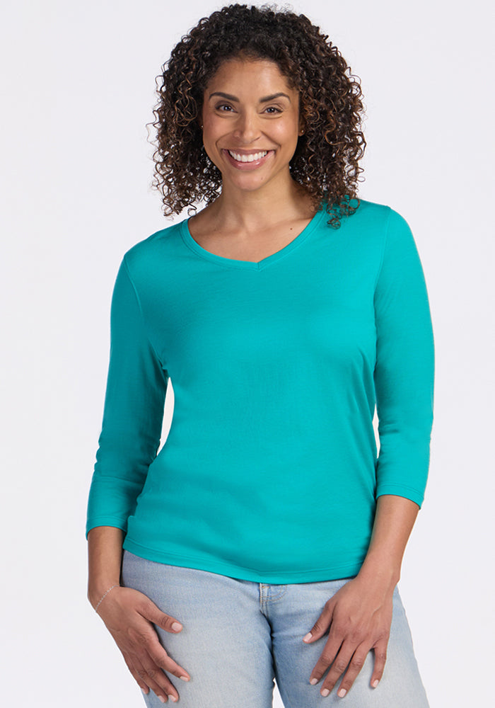 Smiling woman with curly hair wears Woolx Elena 3/4 Sleeve V Neck in Cool Jade and light blue jeans.