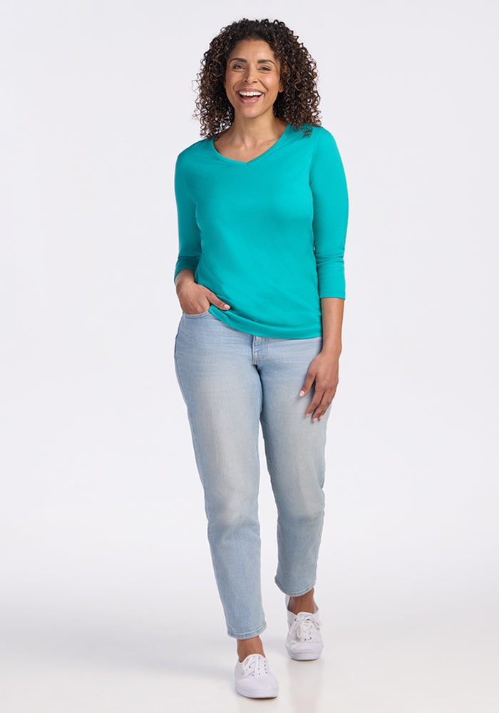 Woman wearing a Woolx Elena 3/4 Sleeve V Neck in Cool Jade and light jeans, smiling with one hand in her pocket.